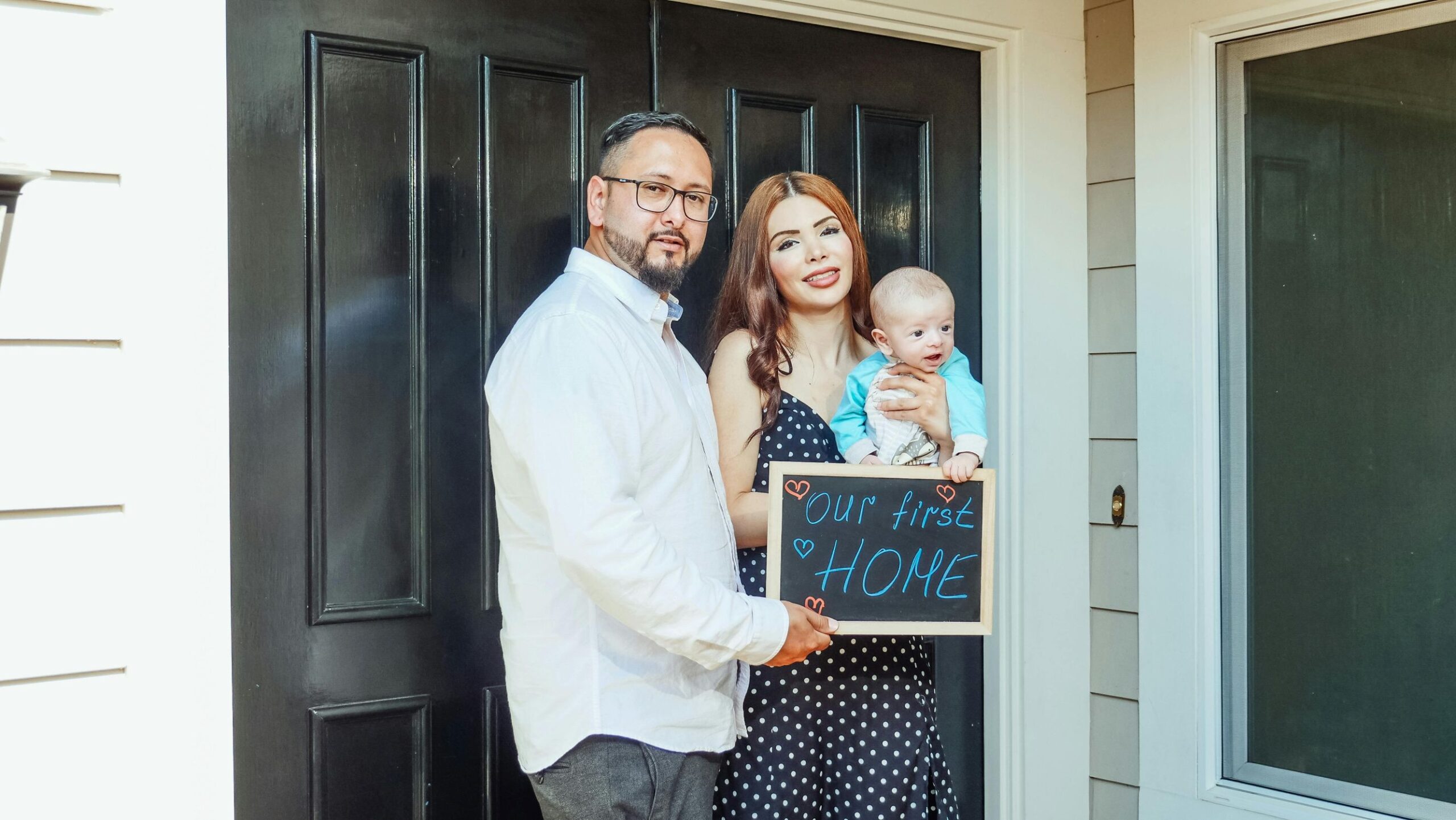 family with sign our first home standing infront of house.