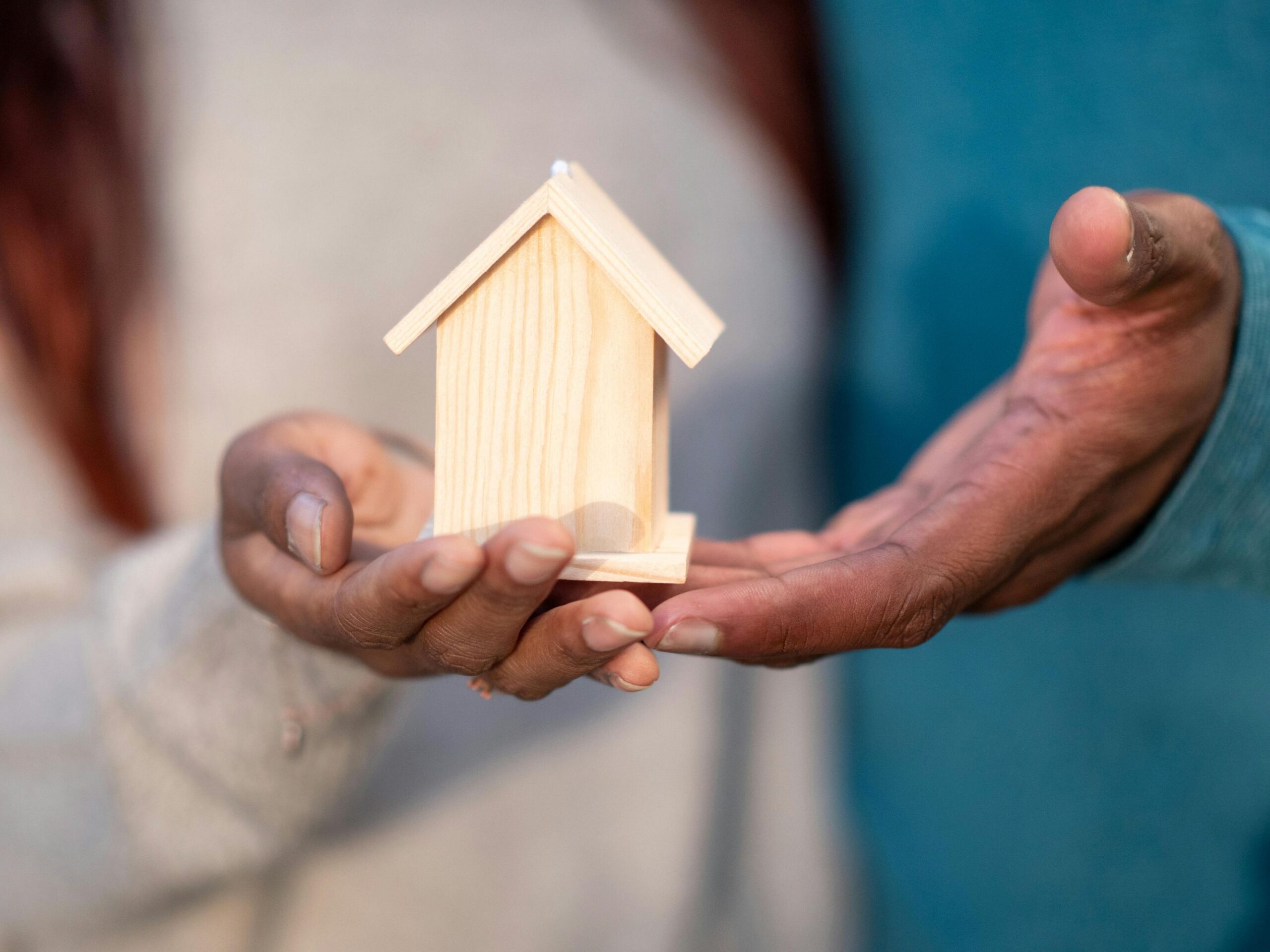Hands holding a miniature house.