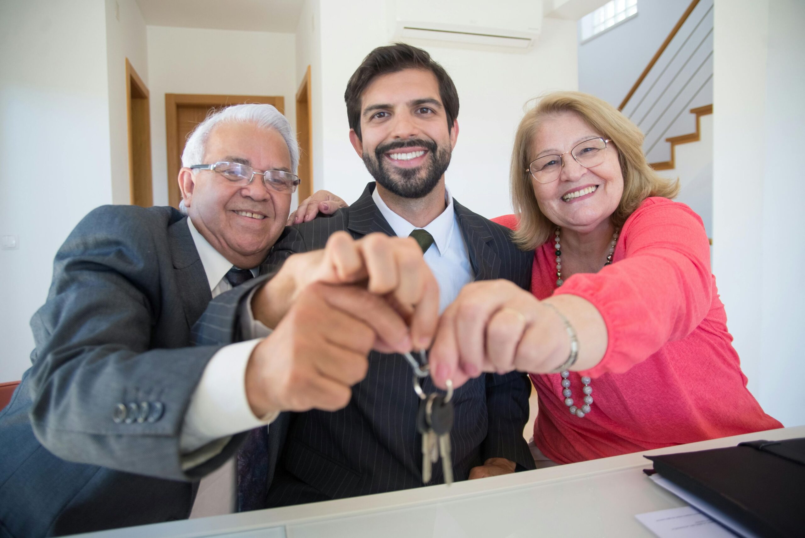 Retired elderly couple holding out house keys with a male real estate agent in the middle of them.