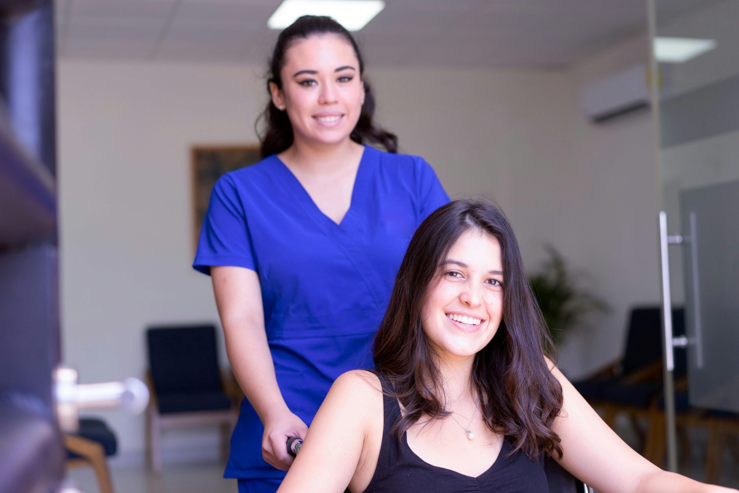 A female nurse is wheeling a smiling female patient on a wheelchair.