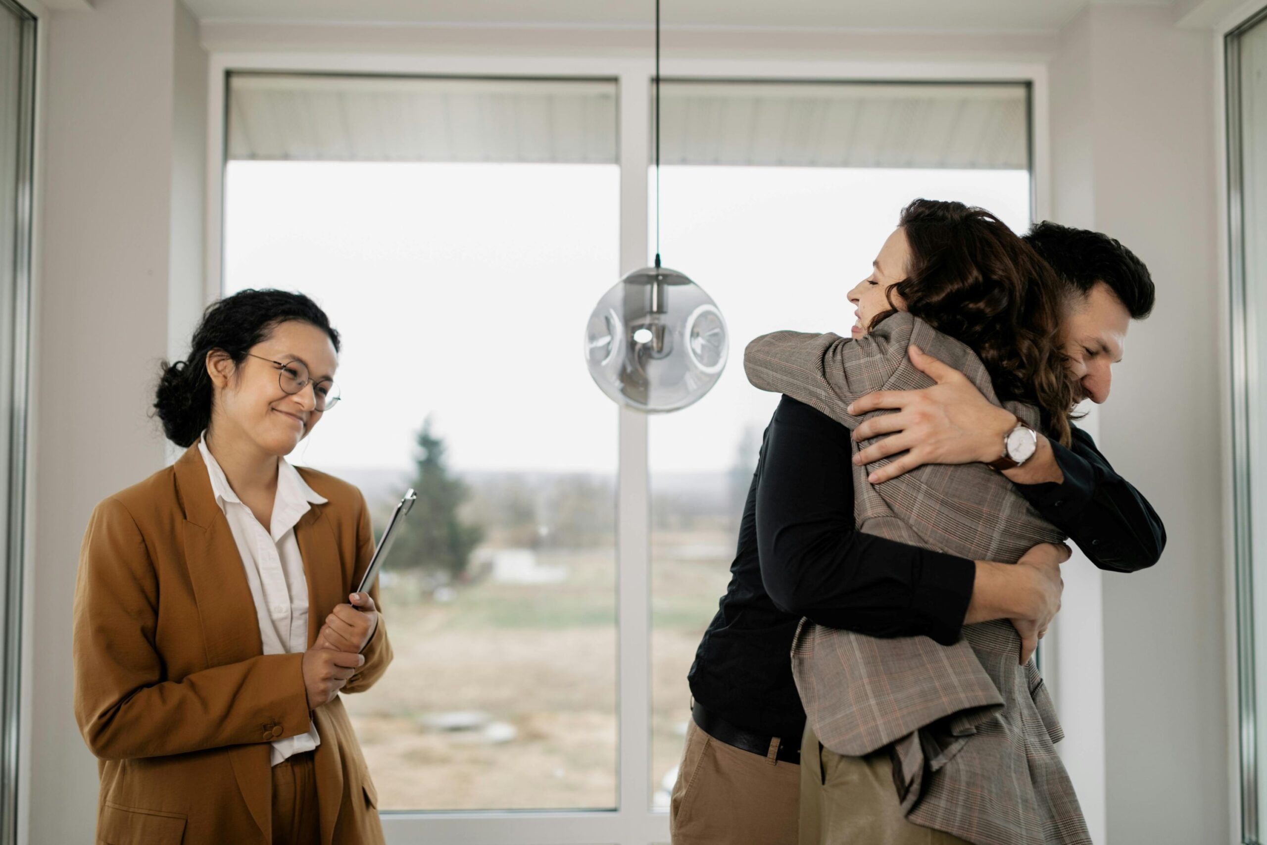A couple hugging, while a female real estate agent is smiling.