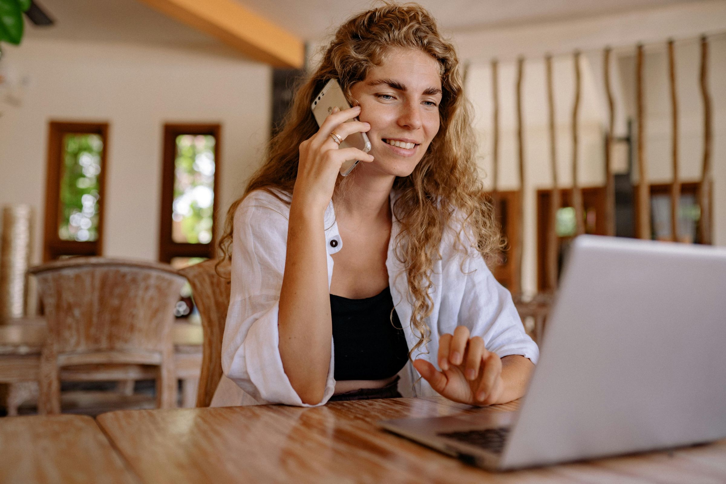 A self-employed freelancer woman working on a laptop while talking on her phone.