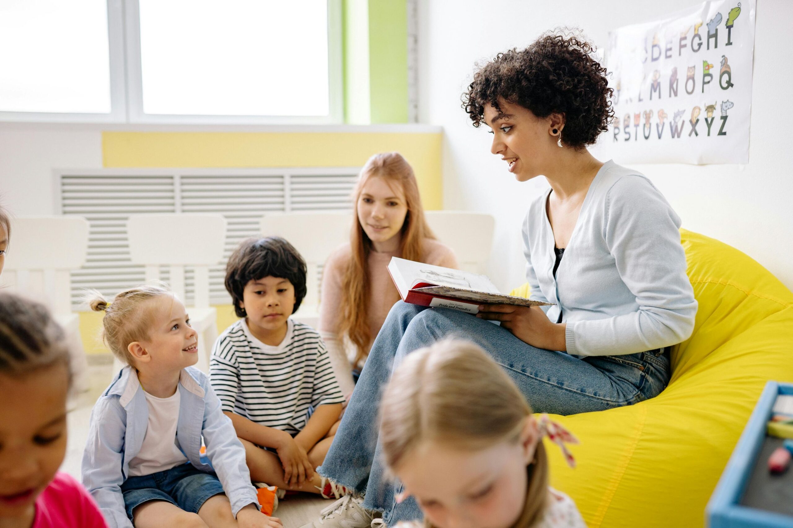 A female teacher sitting and teaching children inside a classroom.