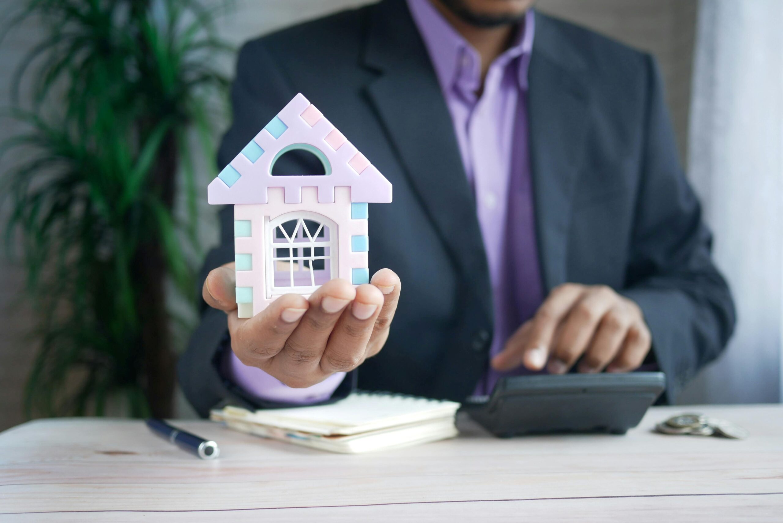 Male holding out in one hand a miniature house model.