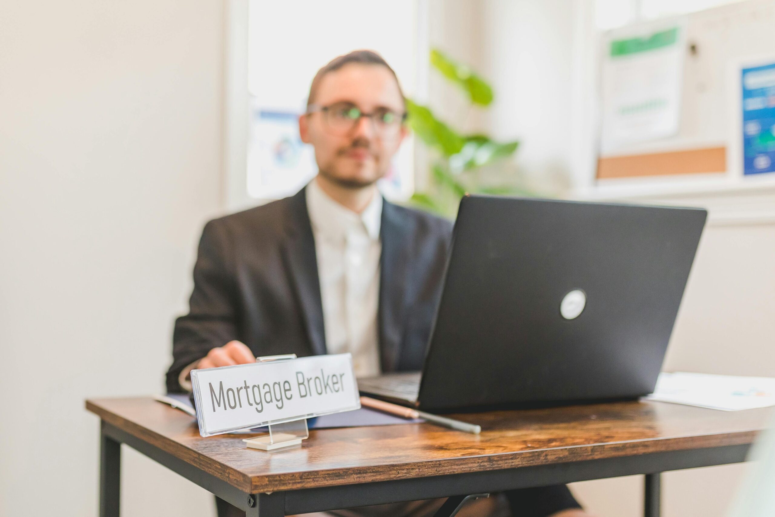 A male broker sitting on a desk, with a sign on the table says mortgage broker.