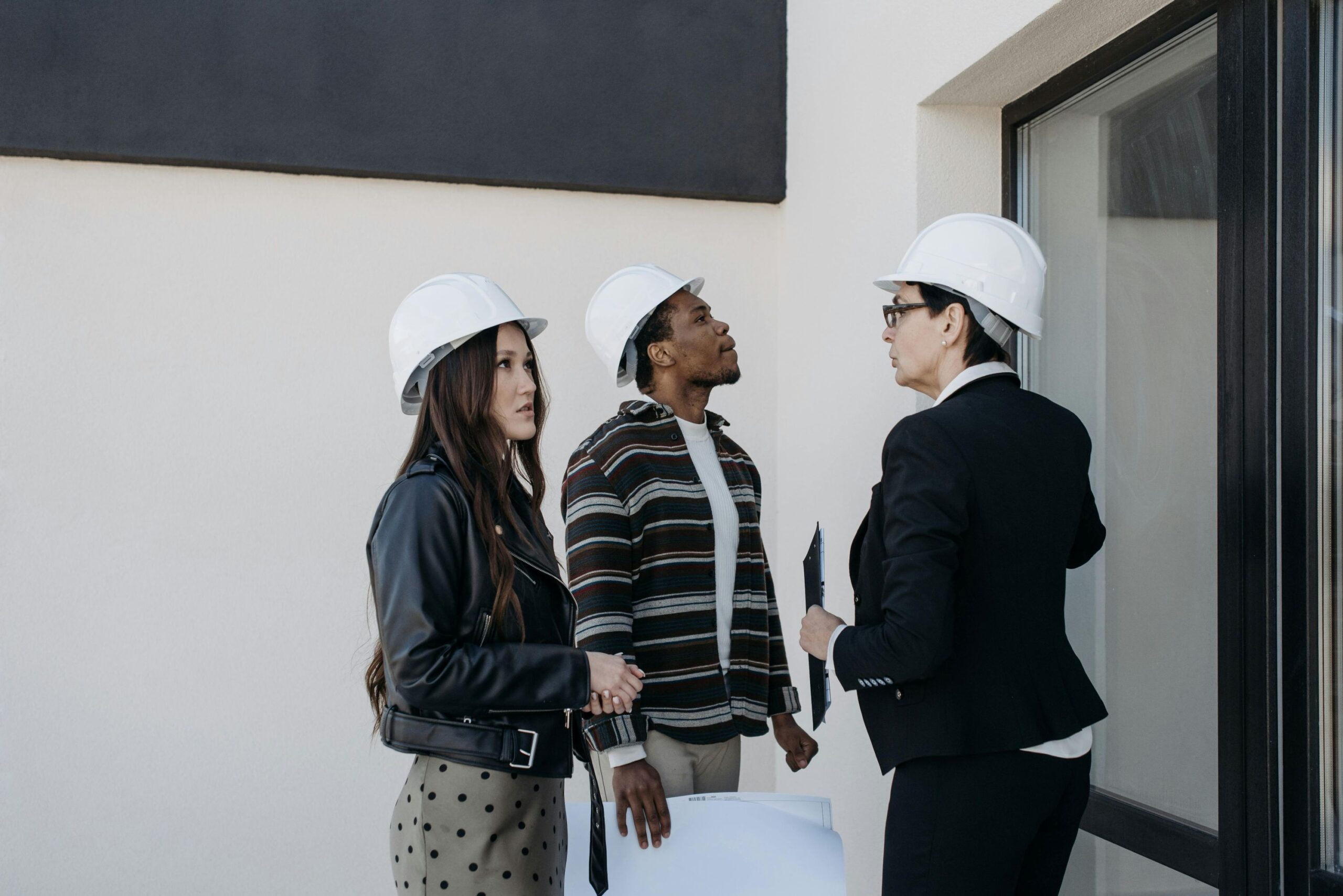 Three person wearing hard hats inspecting a house from the outside.