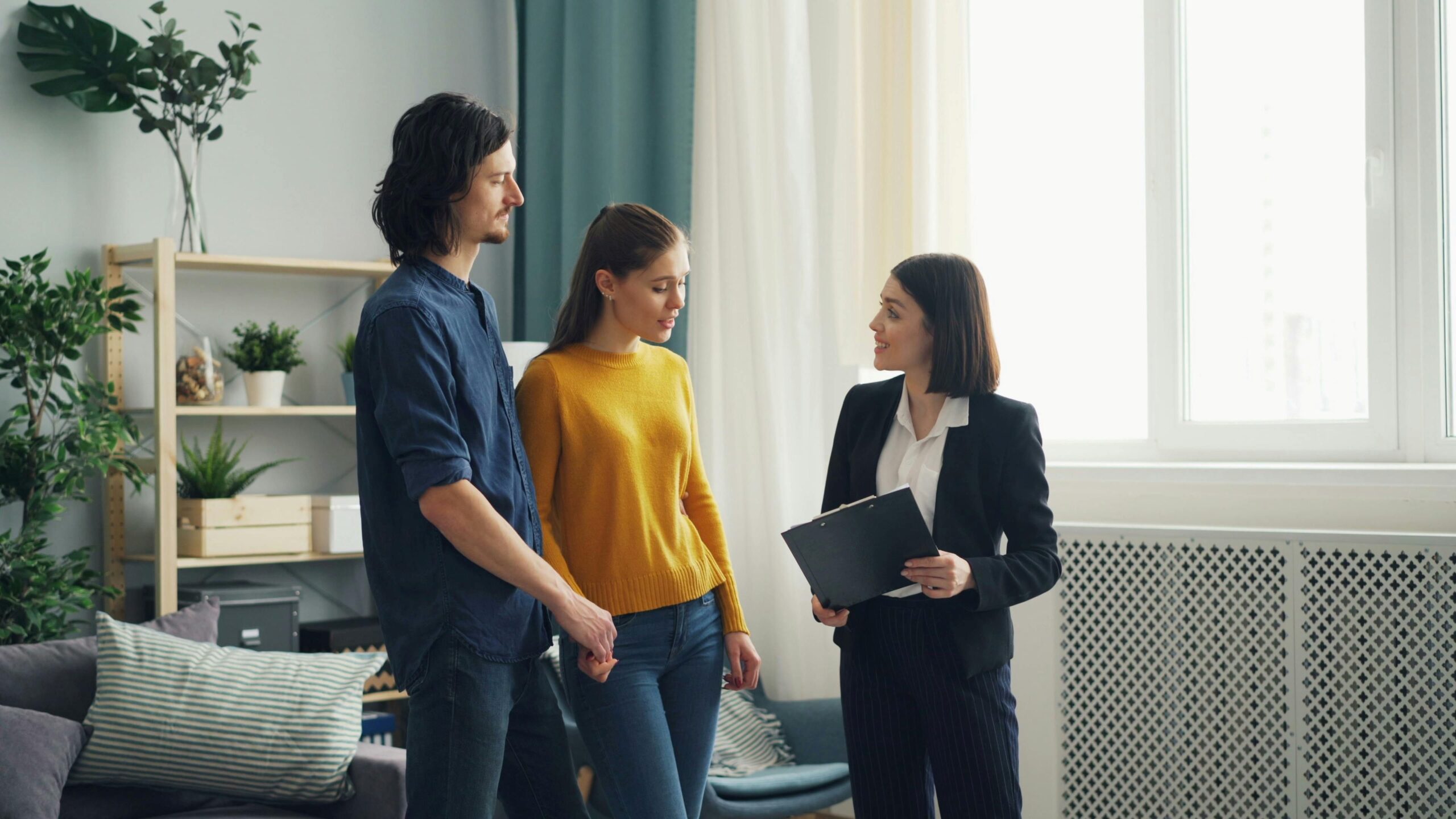 Three persons standing while talking inside a living room.