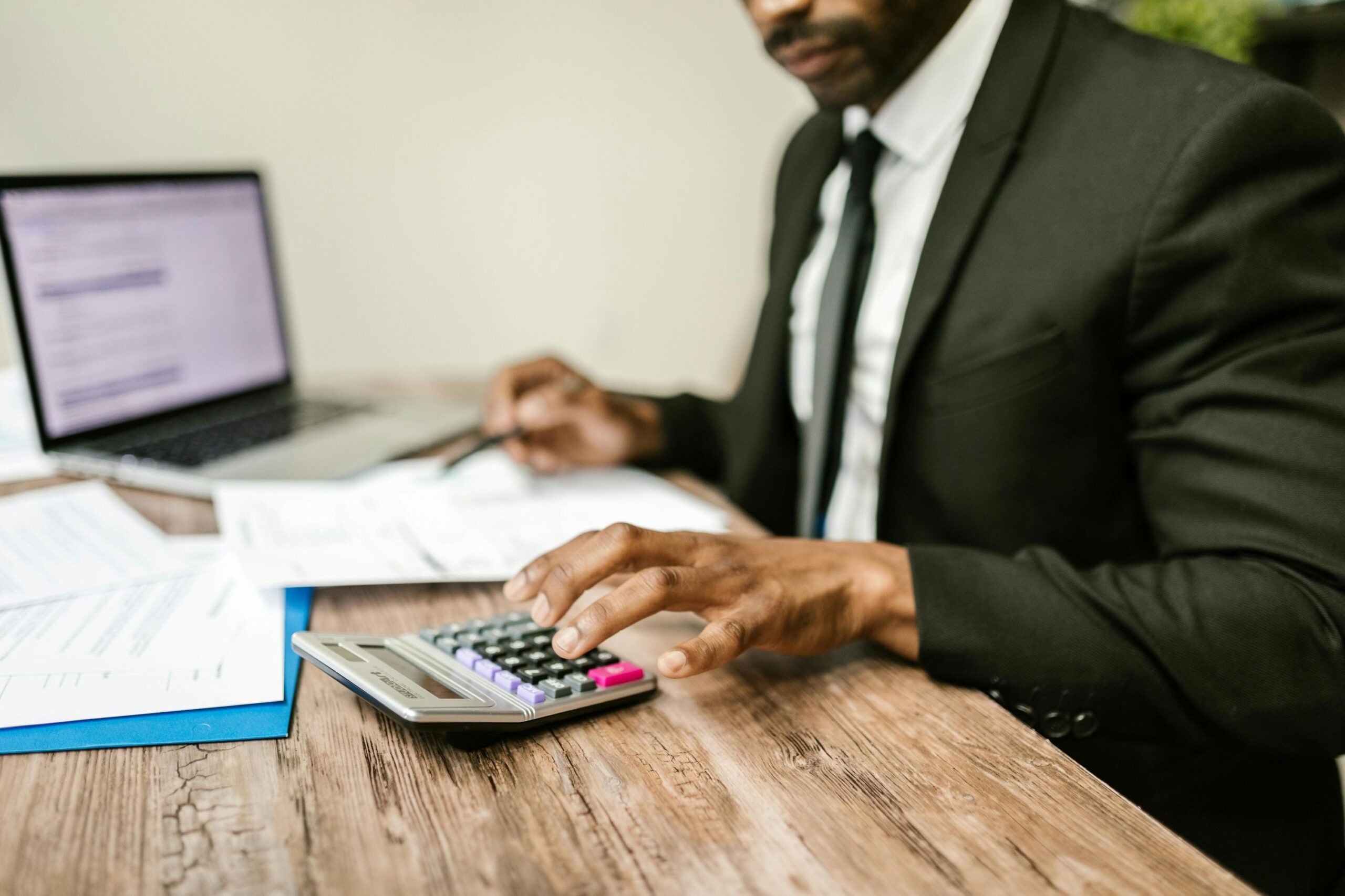 A male in a suit working on his desk, and using a calculator.
