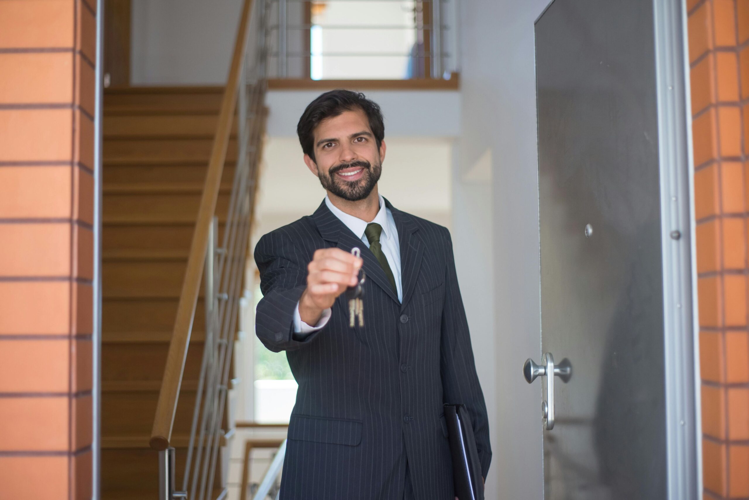 A man in black suit standing by the door while holding up the house key.