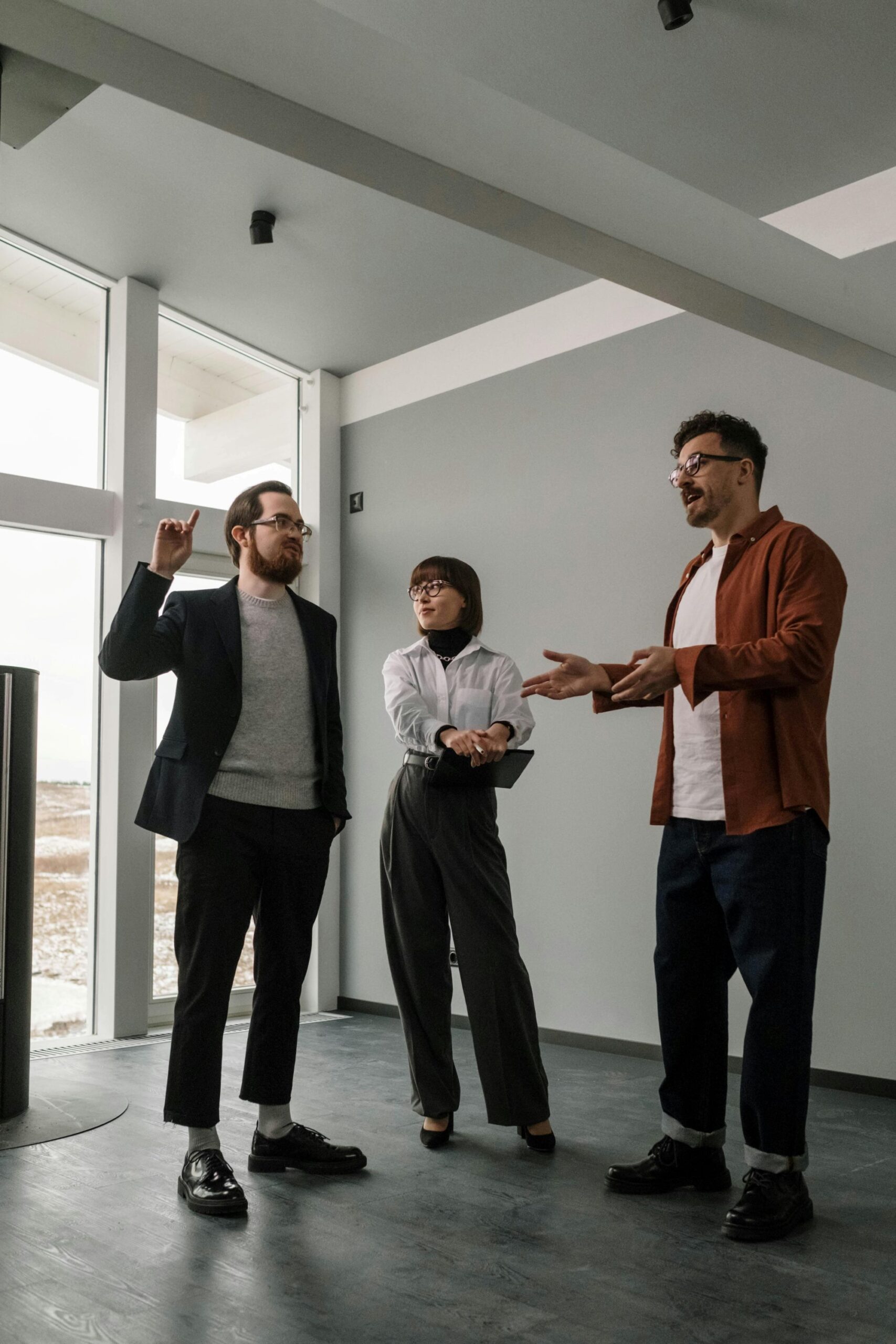 Three persons having a discussion inside an empty apartment.