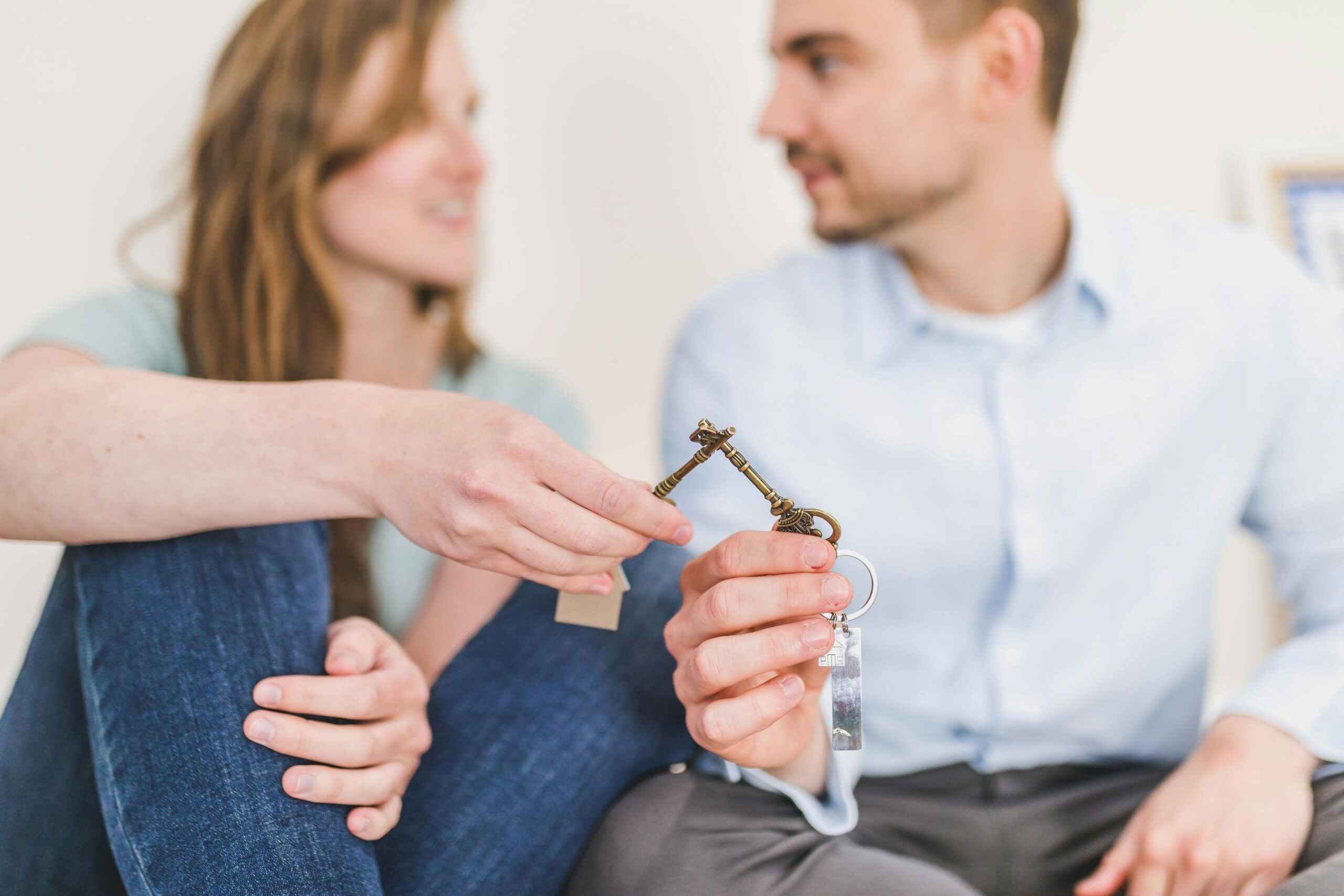 A couple holding up a house key together while sitting.