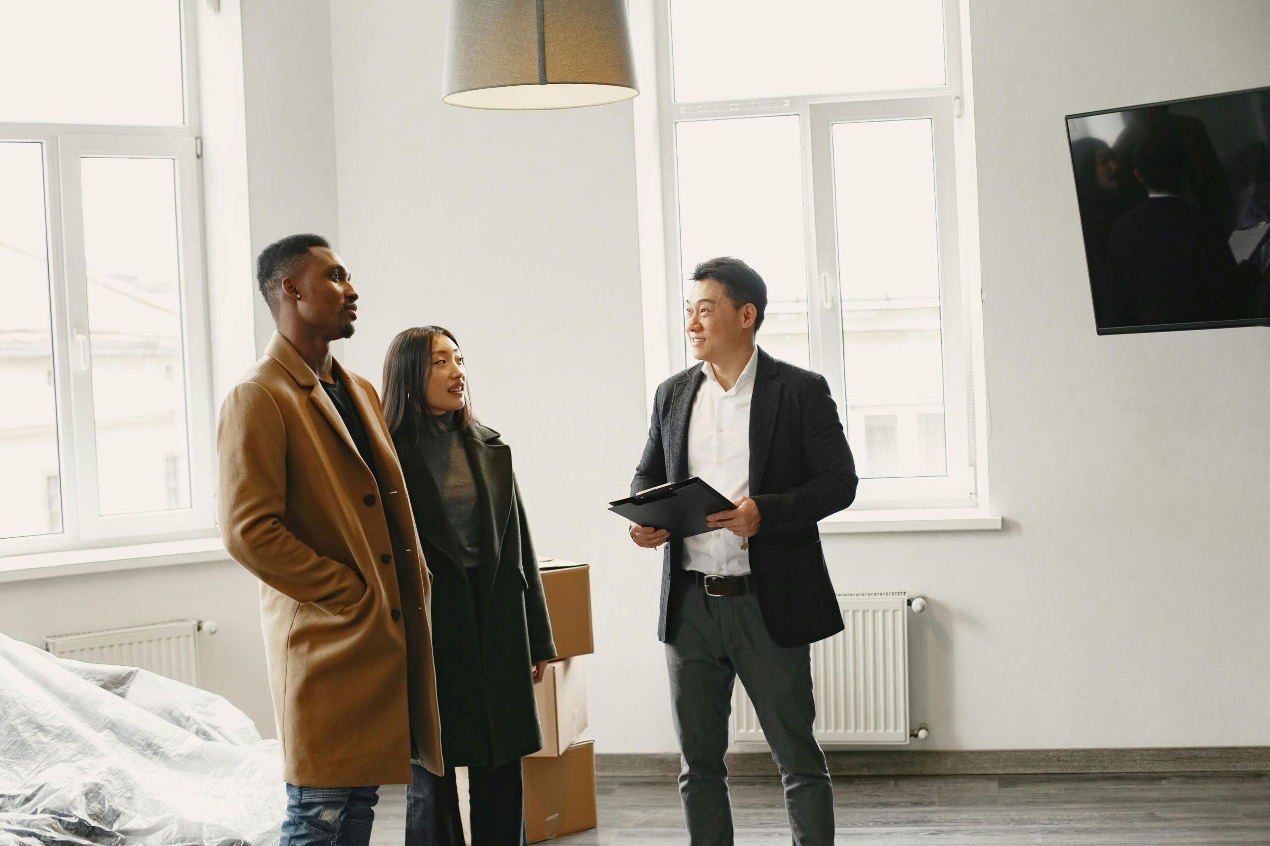A couple in a discussion with a male agent inside an empty apartment.